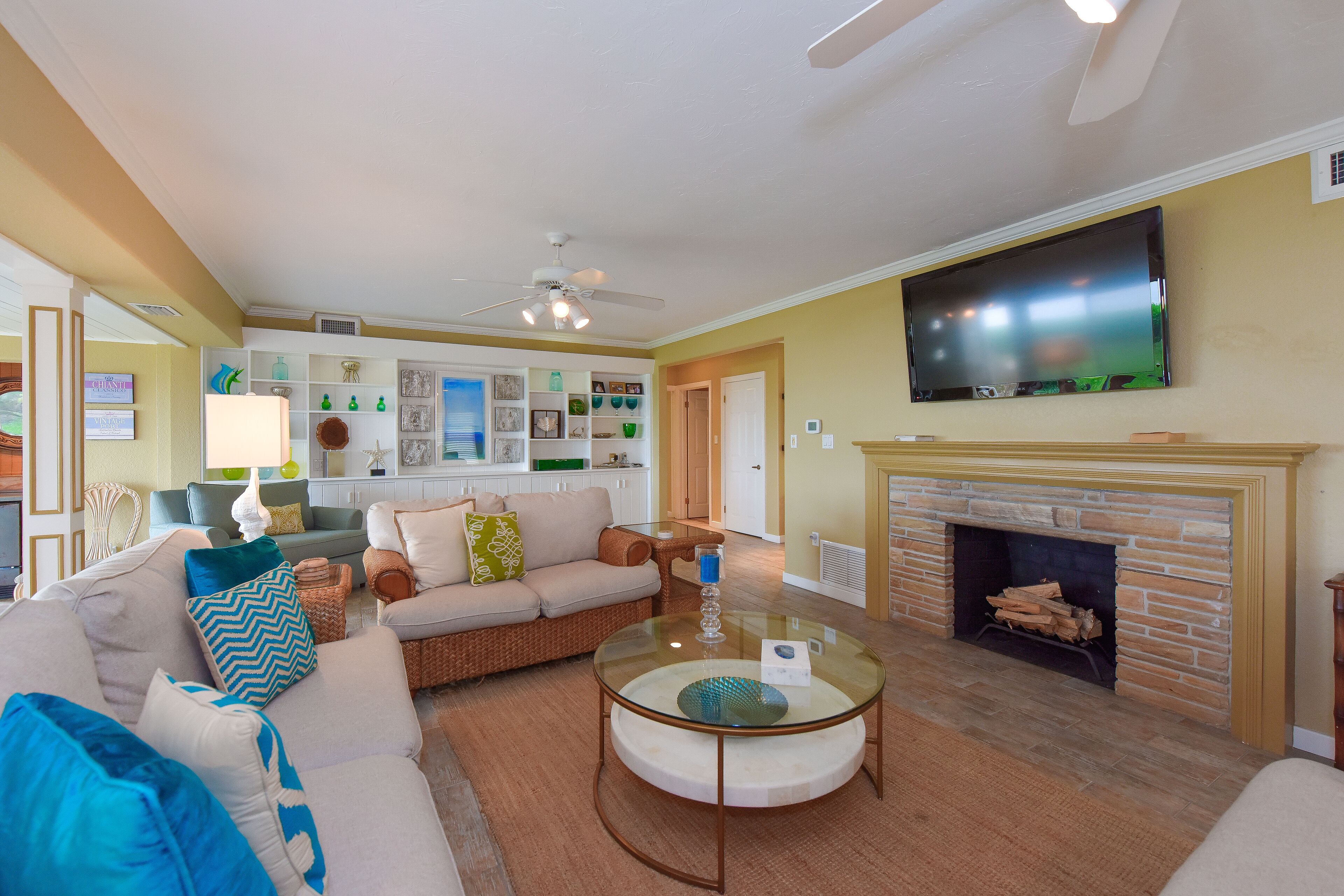 A living room with a fireplace, a television mounted above it, and a ceiling fan.