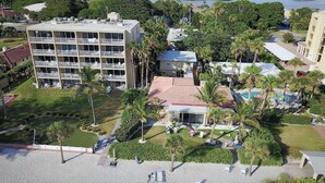 A multi-story hotel with a rooftop pool, surrounded by palm trees and a well-maintained lawn.