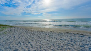 A beach with visible footprints in the sand, a clear sky, and the ocean in the background.