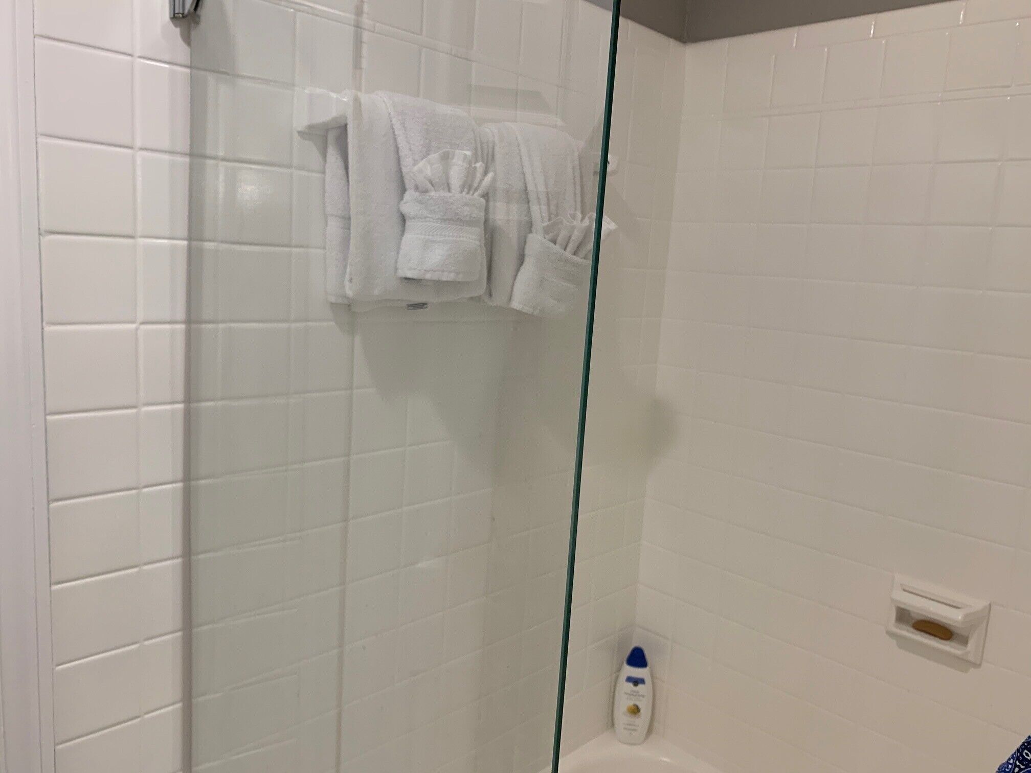A bathroom with white tiled walls, a glass shower enclosure, and a white bathtub.
