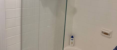 A bathroom with white tiled walls, a glass shower enclosure, and a white bathtub.