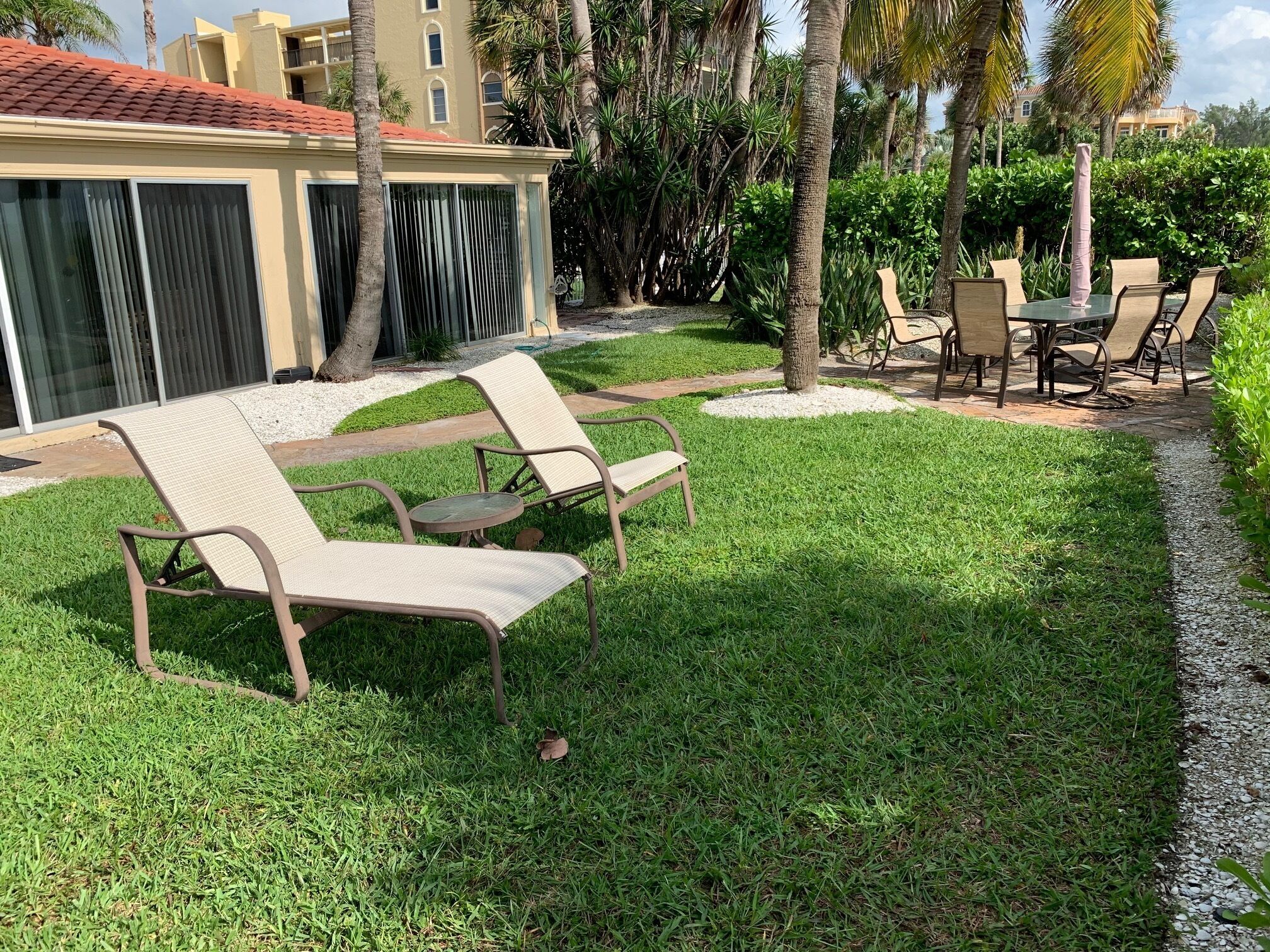Un espacio exterior bien cuidado con dos sillones y una mesa, rodeado de abundante vegetación y palmeras.