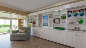 A spacious living room with a grey sofa, wooden flooring, and a white built-in shelving unit with decorative items and framed pictures.