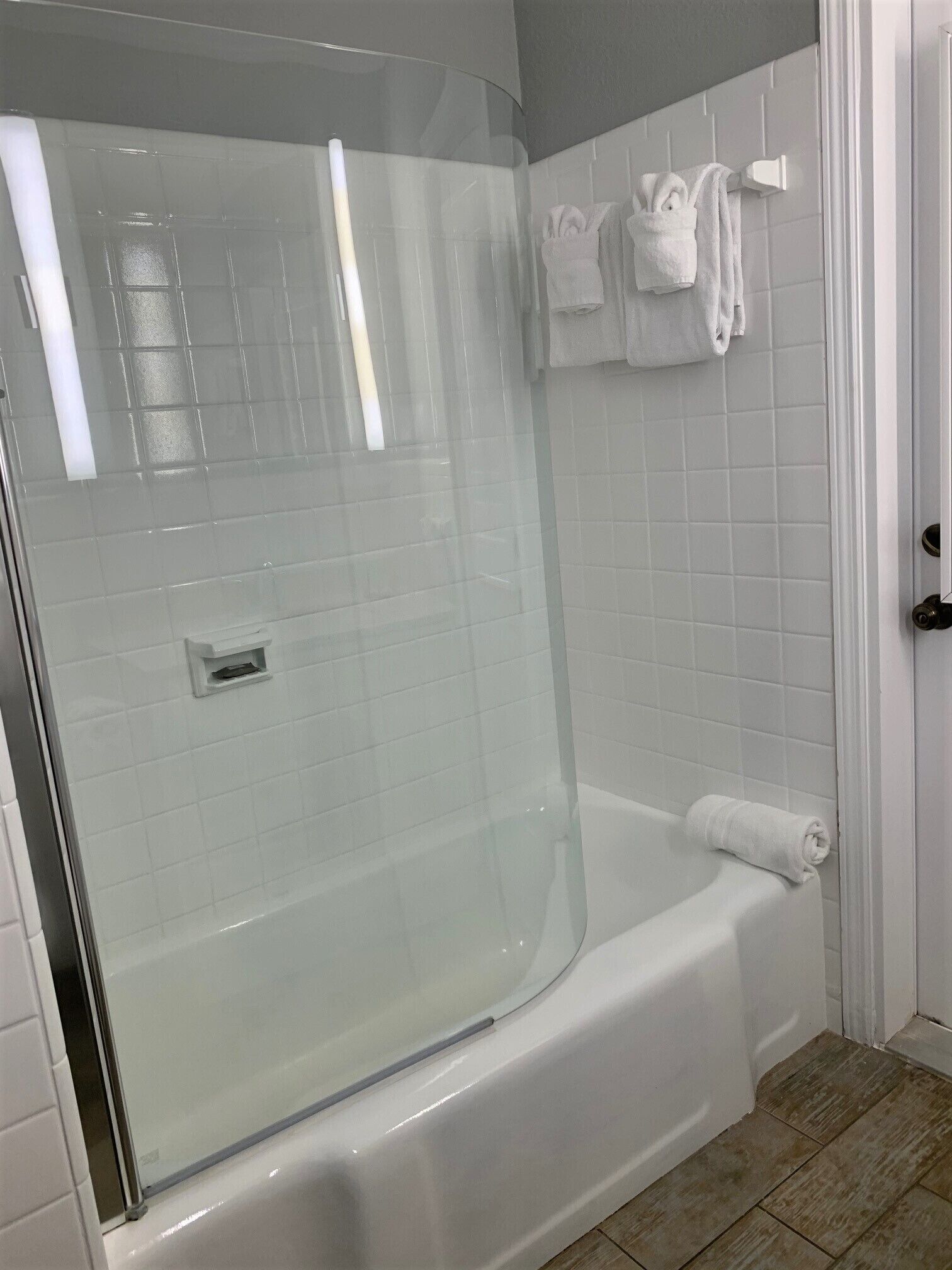 Un baño moderno con ducha de vidrio, una bañera blanca y un muro de azulejos con toallas colgadas en un perchero.