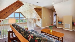Ein Loft-Zimmer mit schräg verlaufender Decke, einer Holzbänkl, einem Tisch und Blick durch große Fenster.