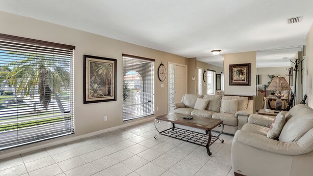 A spacious living room with a beige sofa set, a coffee table, and large windows with blinds. - Beautiful Water Views, 9-min Walk to Beach, 7-min Walk to Restaurants, 5 bikes (Marco Island)