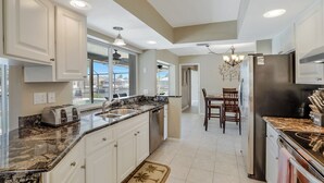 A modern kitchen with white cabinets, granite countertops, a stainless steel refrigerator, and a dining area with a chandelier. - Beautiful Water Views, 9-min Walk to Beach, 7-min Walk to Restaurants, 5 bikes (Marco Island)
