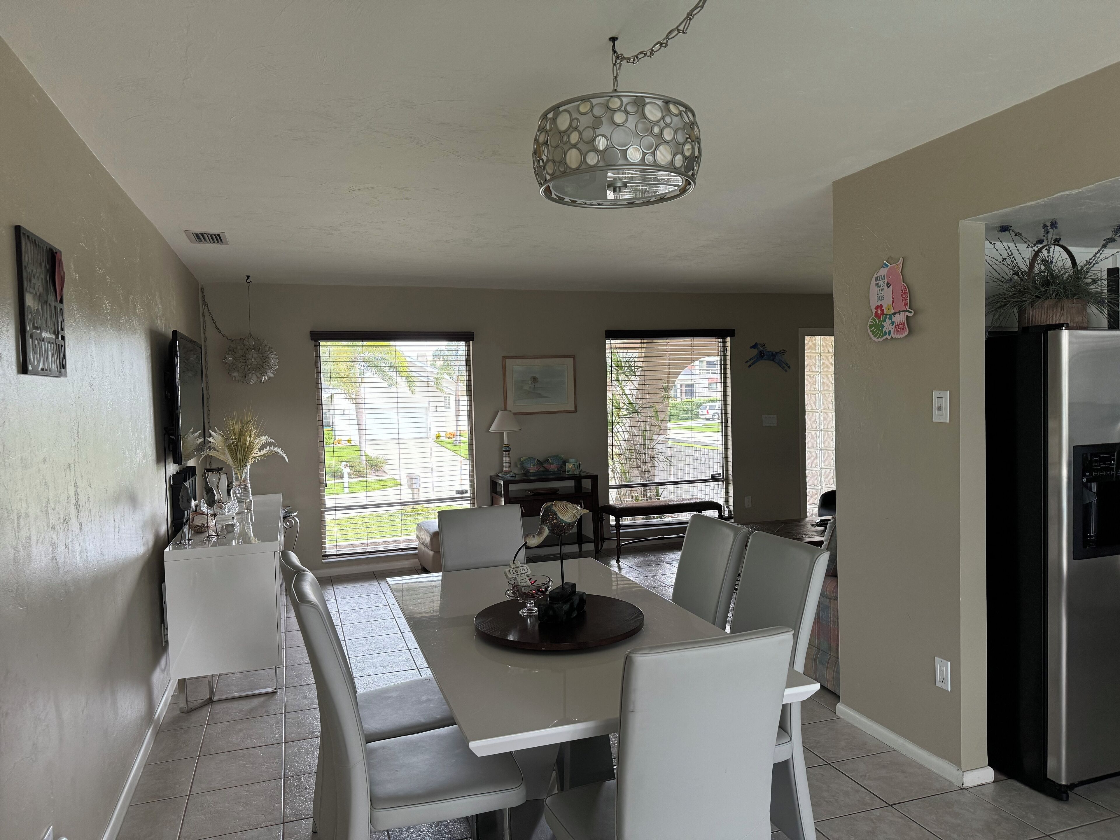 A modern kitchen with a dining area, featuring a large window, a chandelier, and a refrigerator.