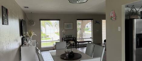 A modern kitchen with a dining area, featuring a large window, a chandelier, and a refrigerator.