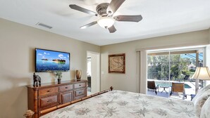 A bedroom with a bed, a ceiling fan, a television, a dresser, and a view of a pool and outdoor seating. - Beautiful Water Views, 9-min Walk to Beach, 7-min Walk to Restaurants, 5 bikes (Marco Island)