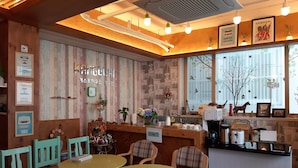 Un café chaleureux, avec des meubles en bois, un comptoir où se trouve une machine à café, et un mur décoré de divers objets et d’une horloge.
