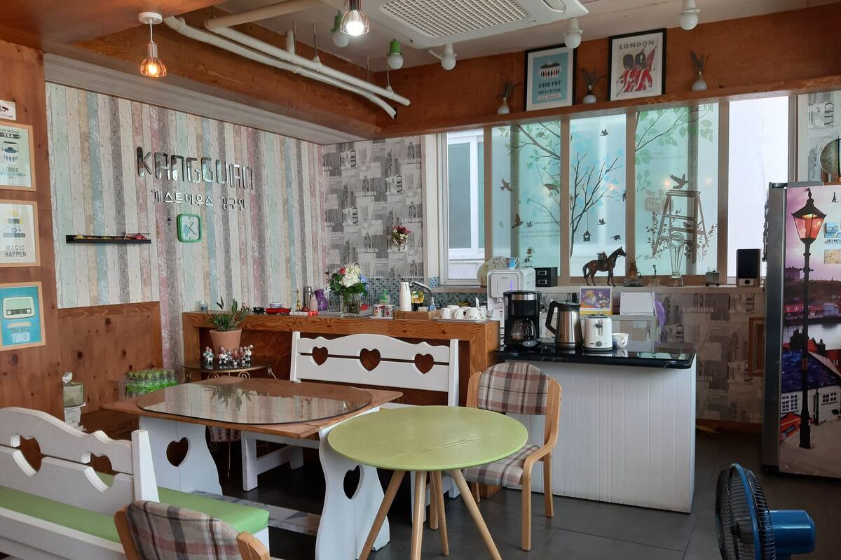 Un café chaleureux, agrémenté de touches de bois, avec une table ronde verte, des chaises en forme de cœur et une vue sur la ville grâce à de grandes fenêtres.