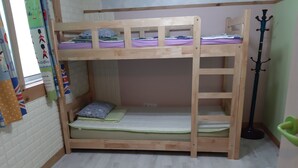 Une chambre avec un lit superposé, une échelle en bois, un lit simple avec un oreiller et un porte-manteau vert.