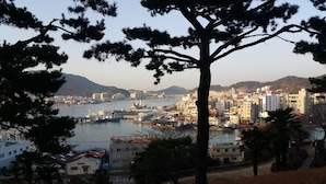 Un paysage urbain côtier avec un arbre imposant au premier plan, un port avec des bateaux, et un mélange de bâtiments résidentiels et commerciaux.