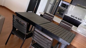 Una cocina moderna con electrodomésticos de acero inoxidable, un comedor con una mesa y sillas de metal negro, y suelo de madera.
