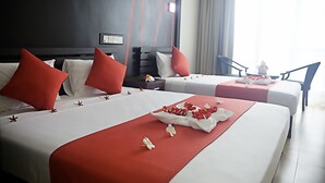 Habitación de hotel con dos camas, ropa de cama roja y blanca, y vistas al exterior.