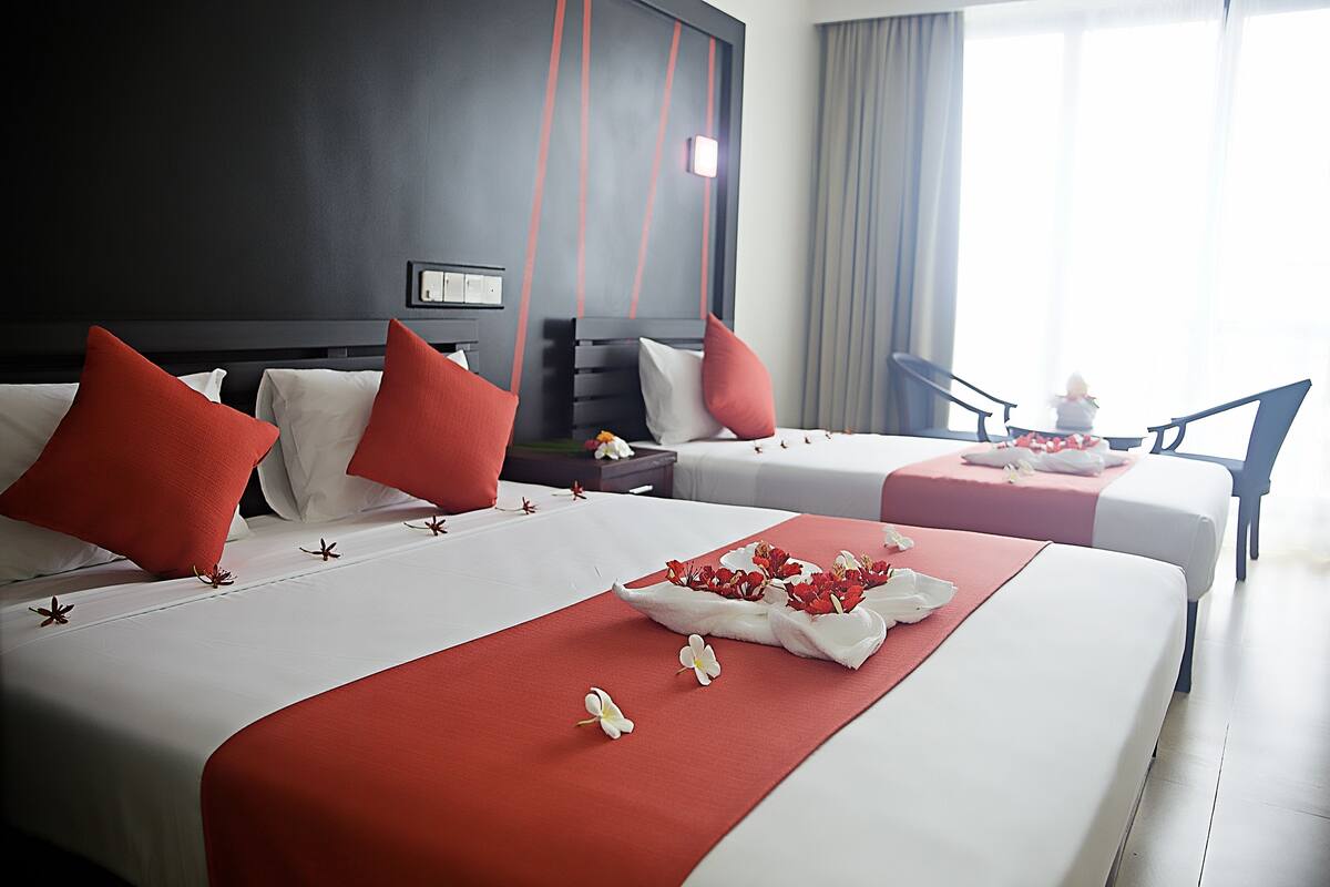 A hotel room with two beds, red and white bedding, and a view of the outdoors.