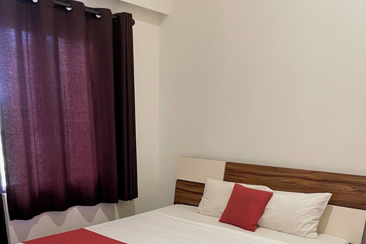 A neatly made bed with white and red bedding, a wooden headboard, and a pair of towels on the footboard.
