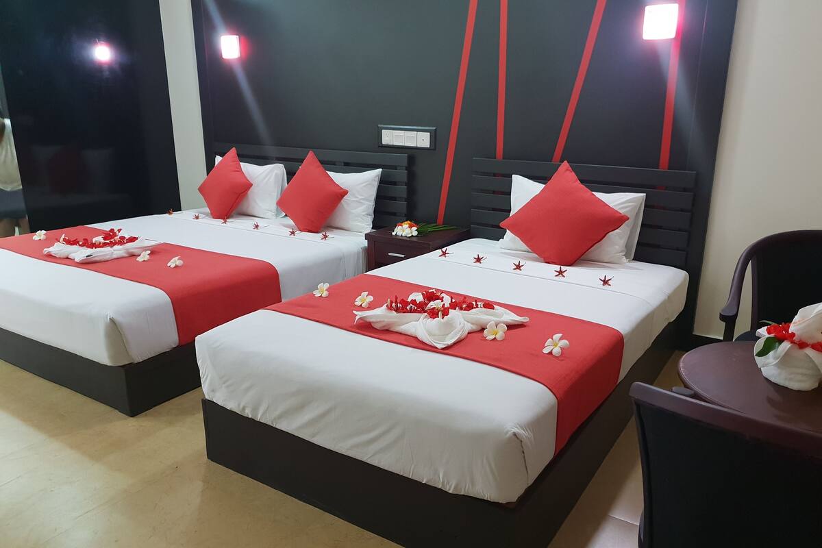 Two neatly made beds with red and white bedding, a nightstand with a lamp, and a chair.