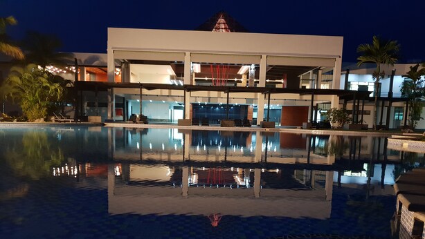 Un hotel moderno con una gran piscina que refleja el edificio y las palmeras.
