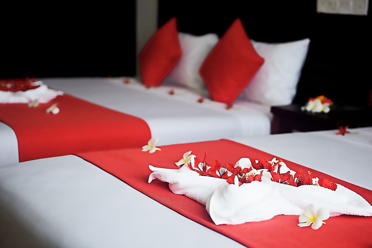 A hotel room with two beds, each with red and white bedding, and a red and white floral arrangement on the beds.