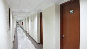 Un largo y estrecho pasillo de hotel con paredes blancas, una puerta de madera a la derecha y un letrero con un número arriba.