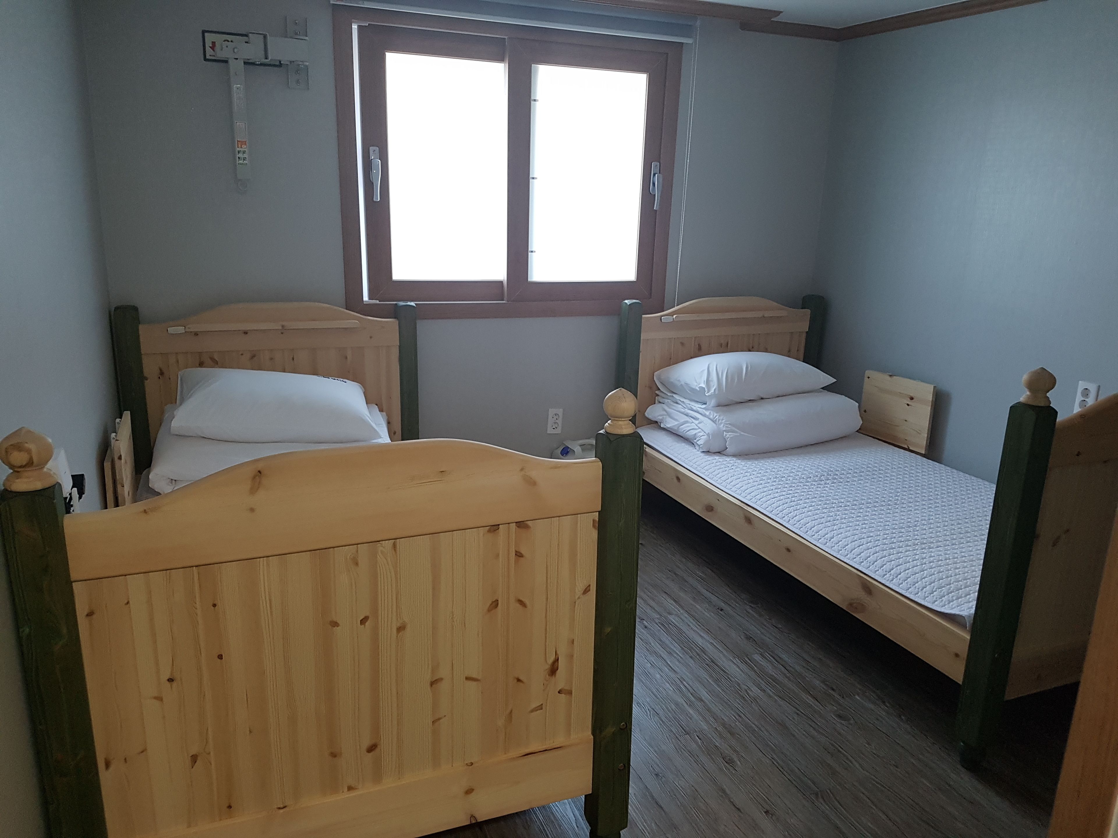 Una habitación con dos camas literas de madera, una ventana con marcos de madera e interruptor de luz fijado a la pared.