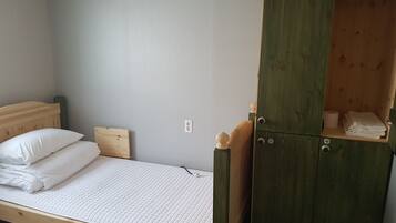 Una cama individual con cabecera de madera y un armario verde con un estante.