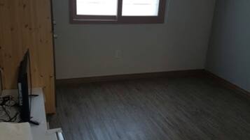 Una habitació amb sòl de fusta, una finestra amb persianes i una porta.