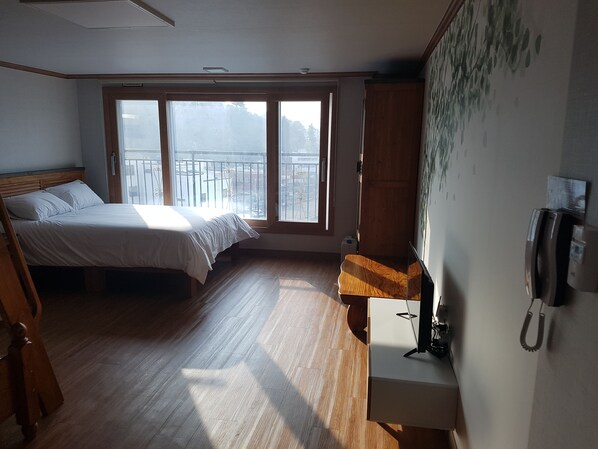 A bedroom with a bed, a desk, a phone, and a window with a view of the outdoors.