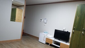 A room with a wooden floor, a white desk with a computer and a TV, a green wardrobe, and a mirror on the wall. - The View Hostel (Tongyeong)
