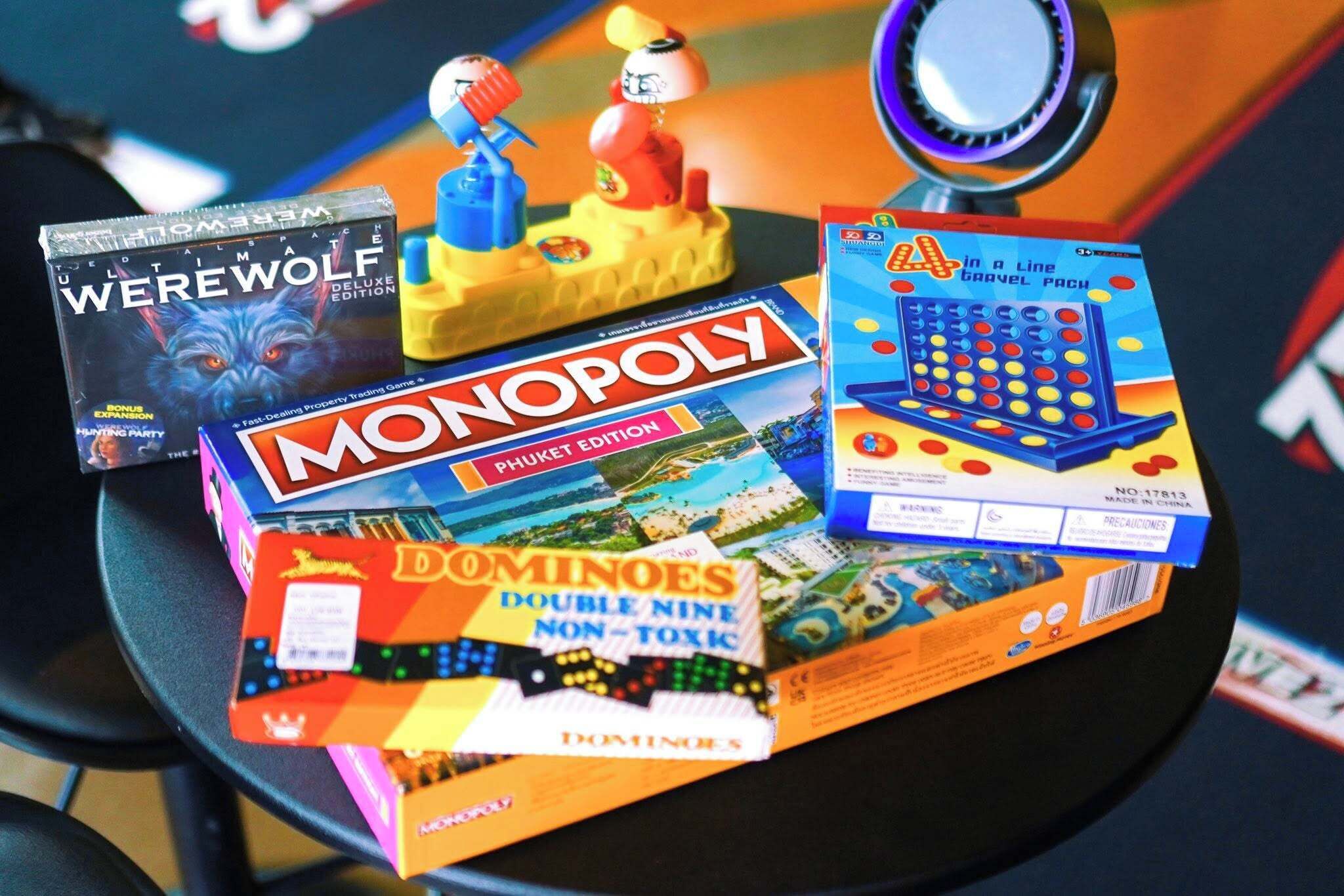 A table with various board games including Monopoly, Werewolf, and Dominoes.