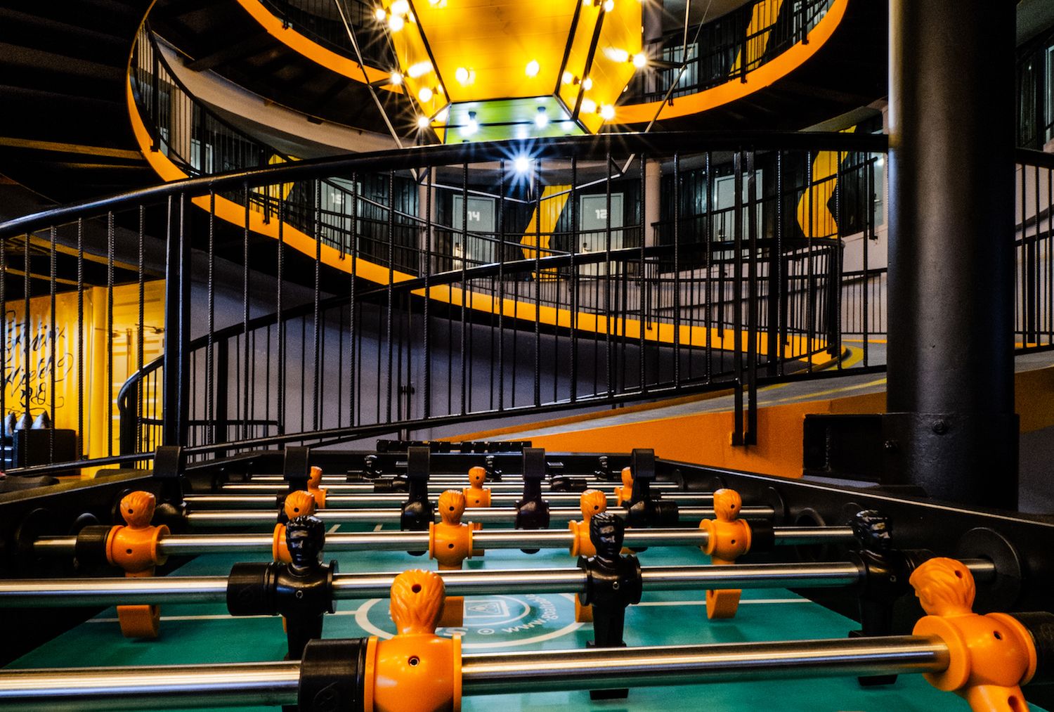 A foosball table in a brightly lit indoor space with a spiral staircase and yellow accents.