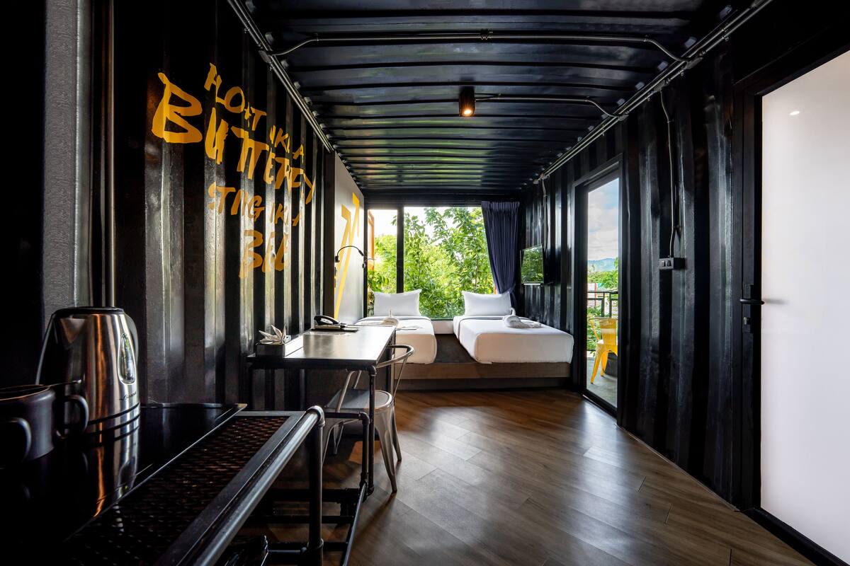 Una habitación moderna con piso de madera, una cama, una mesa con un hervidor y una ventana con vistas a zonas verdes.