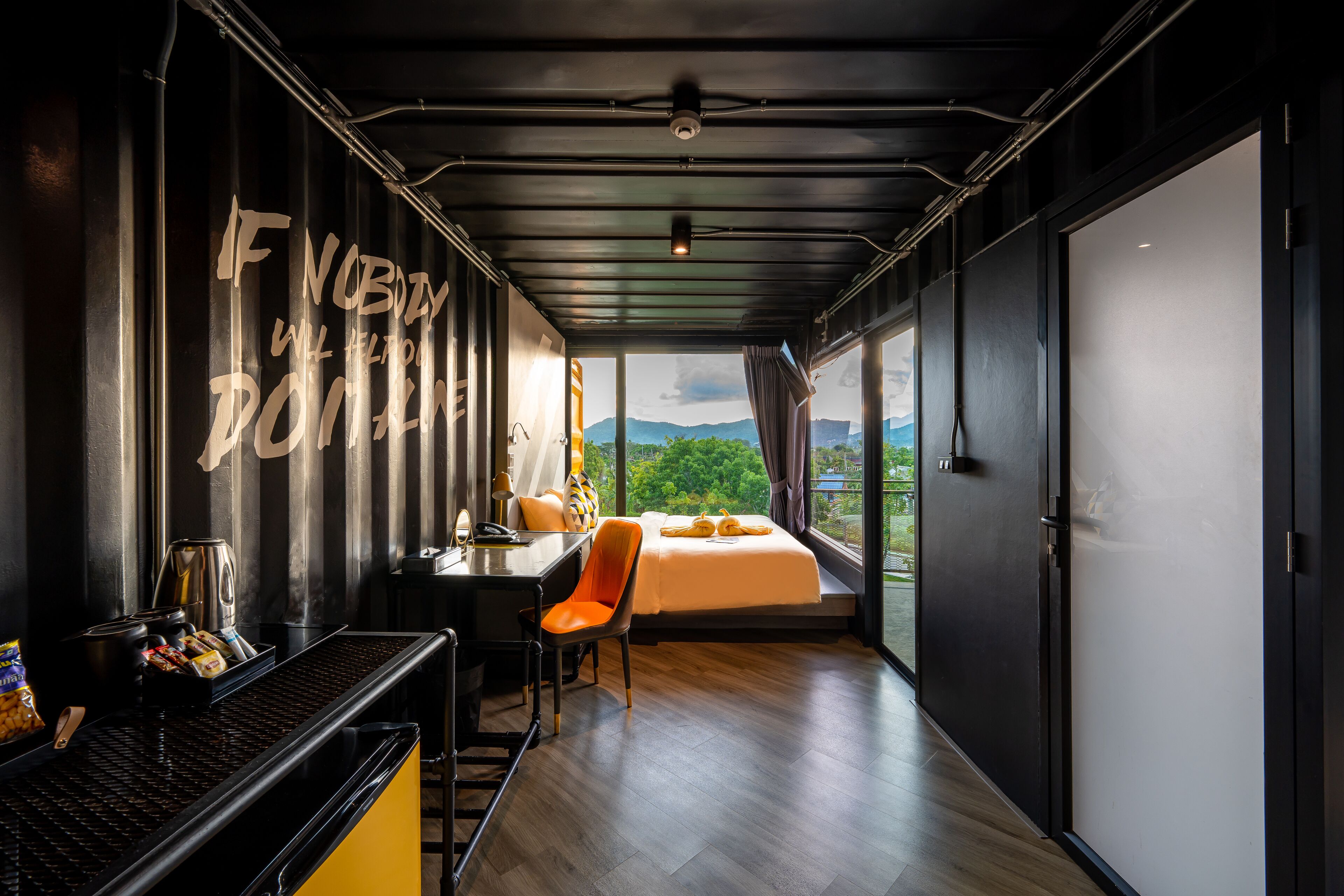 A modern hotel room with a large bed, a desk with a chair, a coffee machine, and a view of the outdoors.