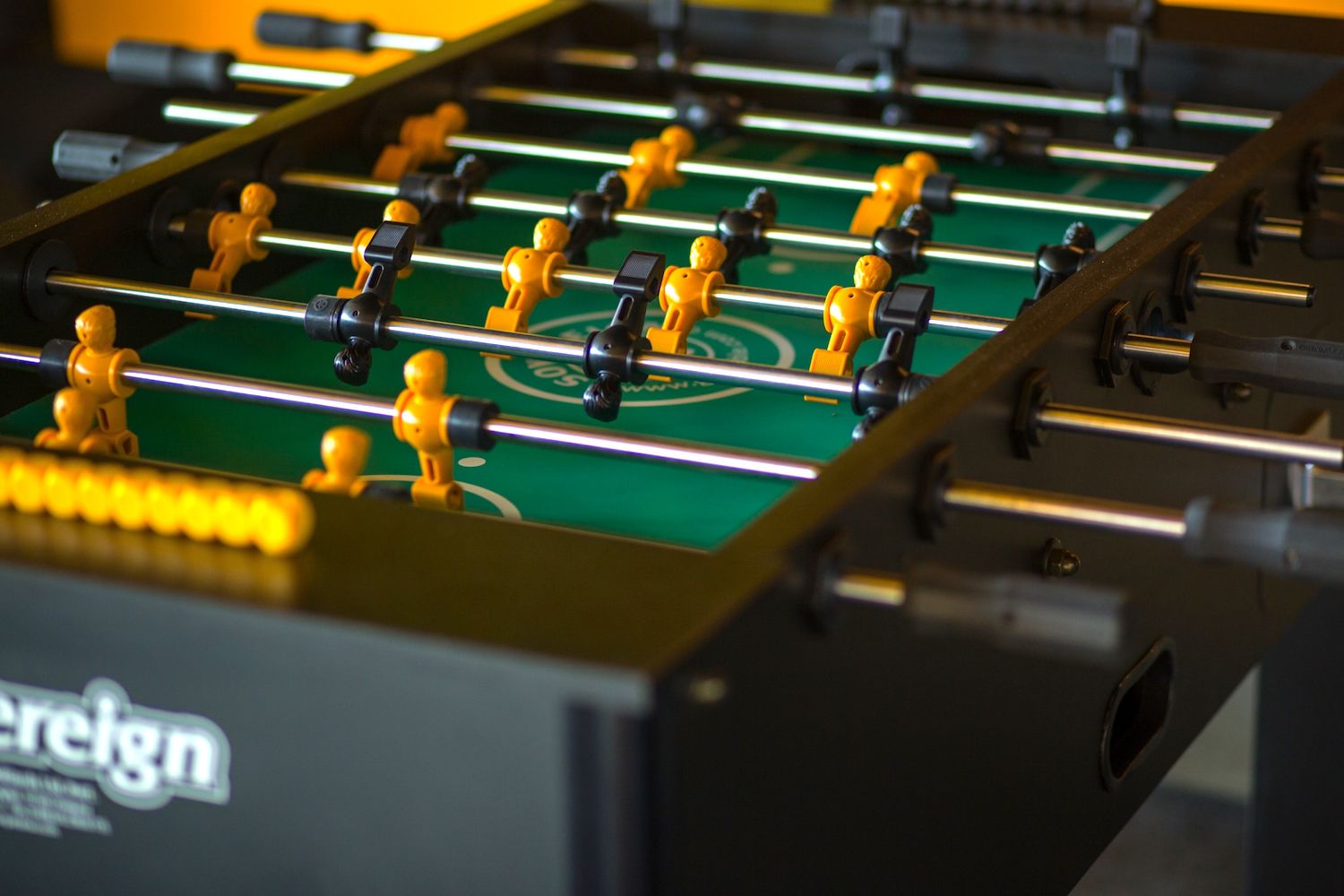 A close-up of a foosball table with a green playing surface and yellow and black player figures.