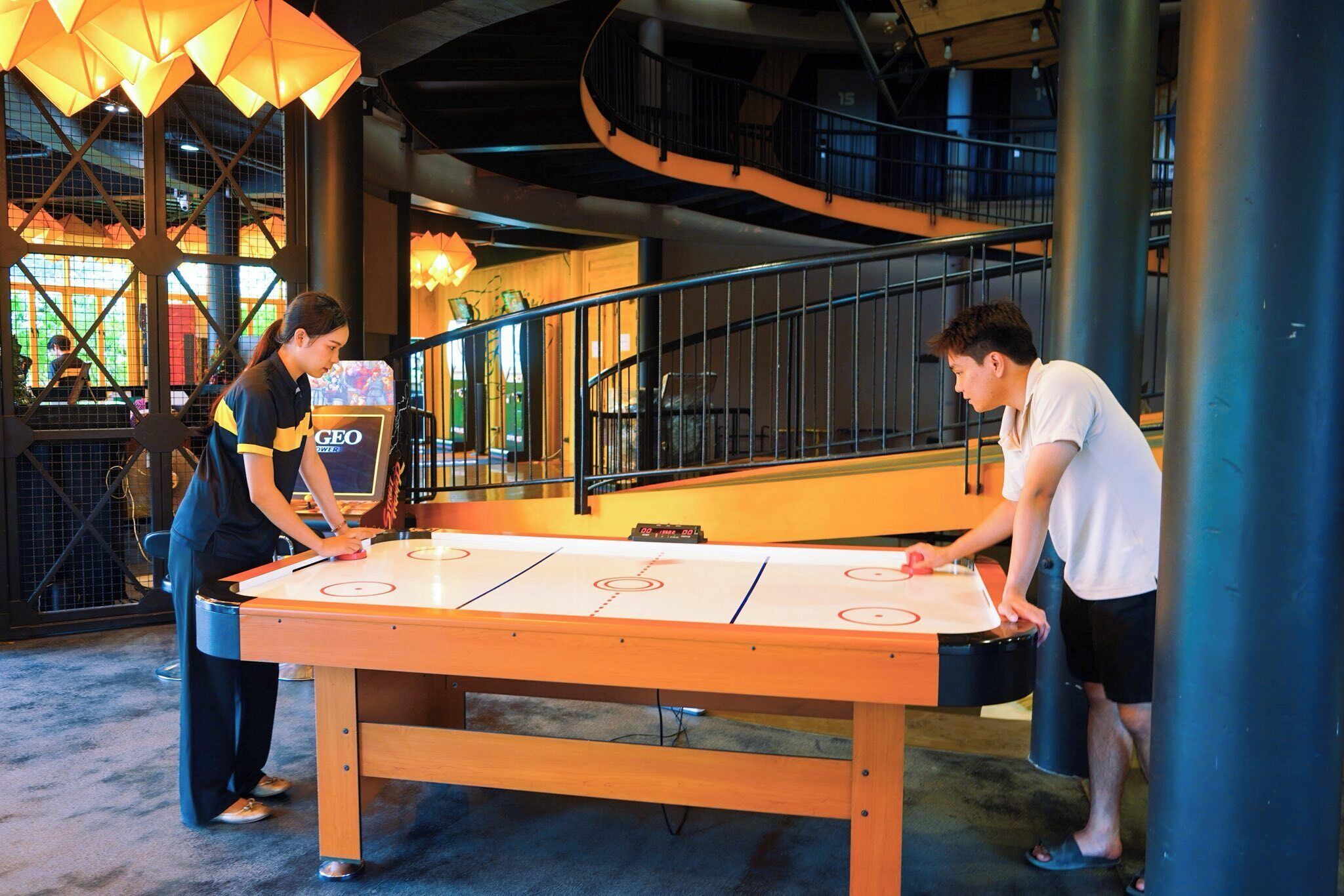 A table hockey game in a modern indoor setting with a staircase and industrial-style lighting.