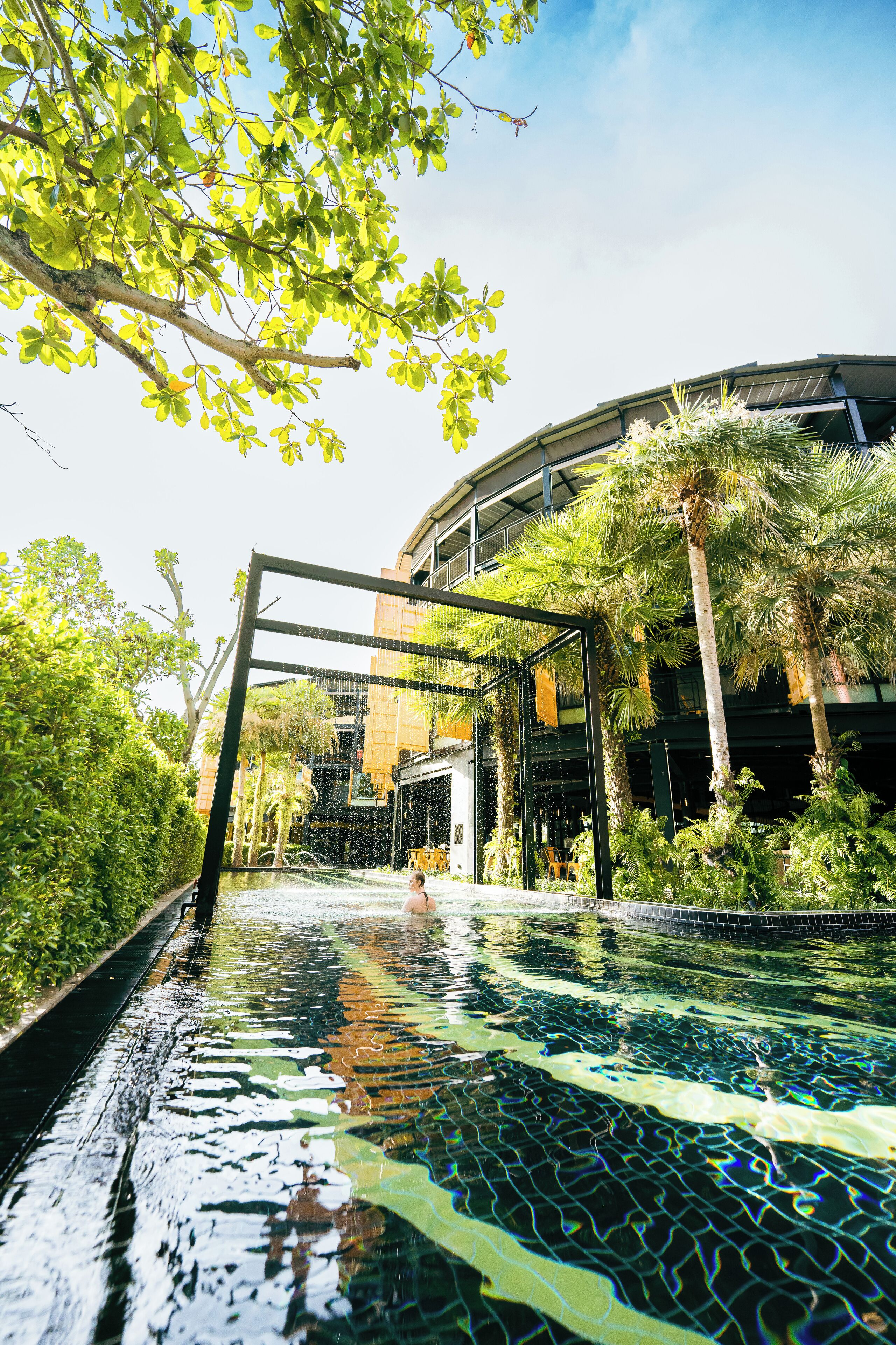An infinity pool with a view of a modern building and lush greenery.