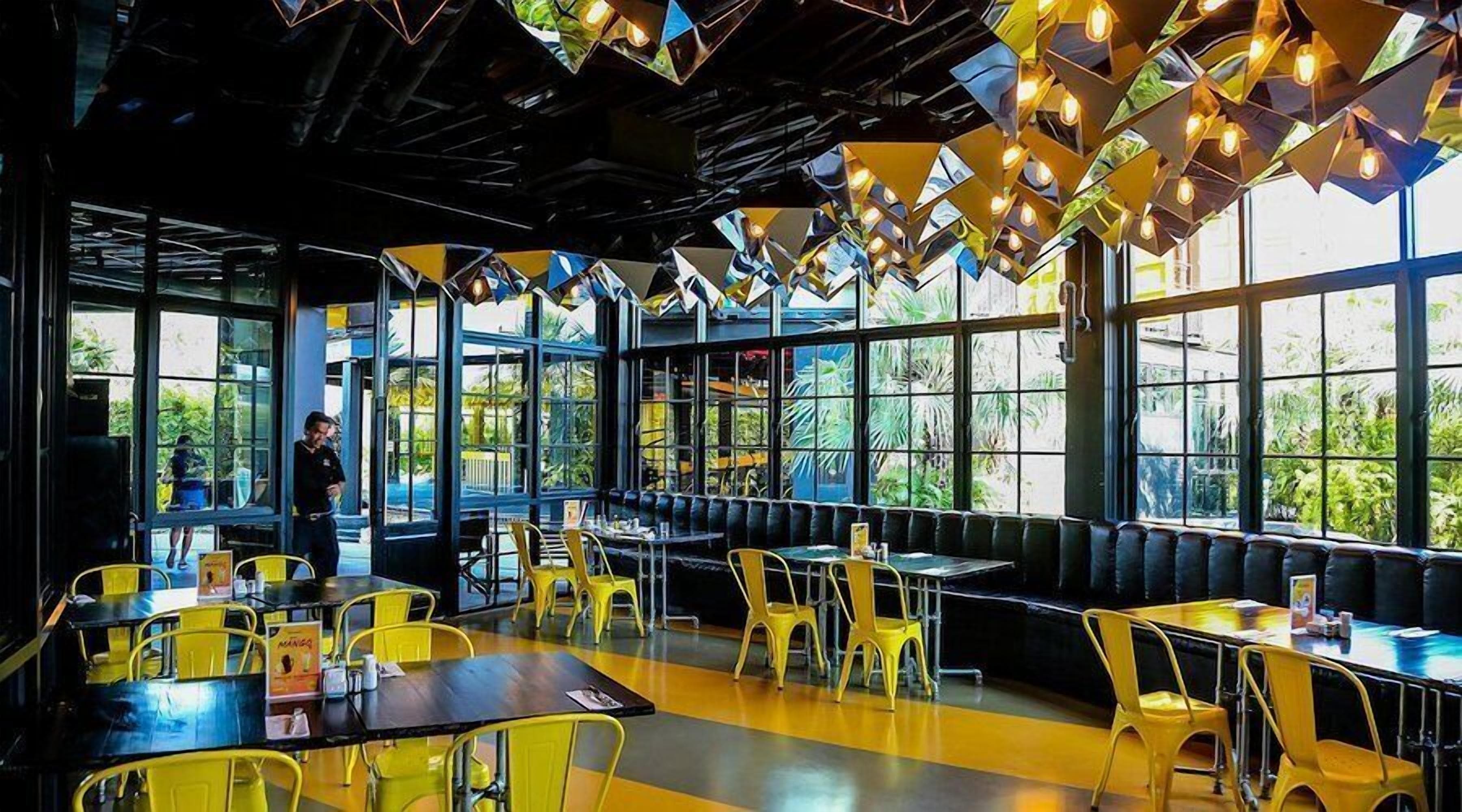 An indoor dining area with yellow chairs and tables, large windows, and a modern ceiling design.