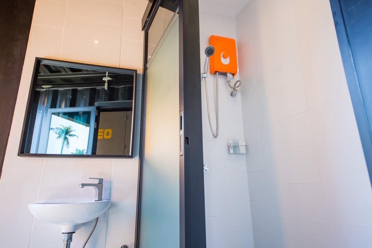Un bagno con un lavandino bianco, uno specchio e una doccia con pannello comandi arancione.