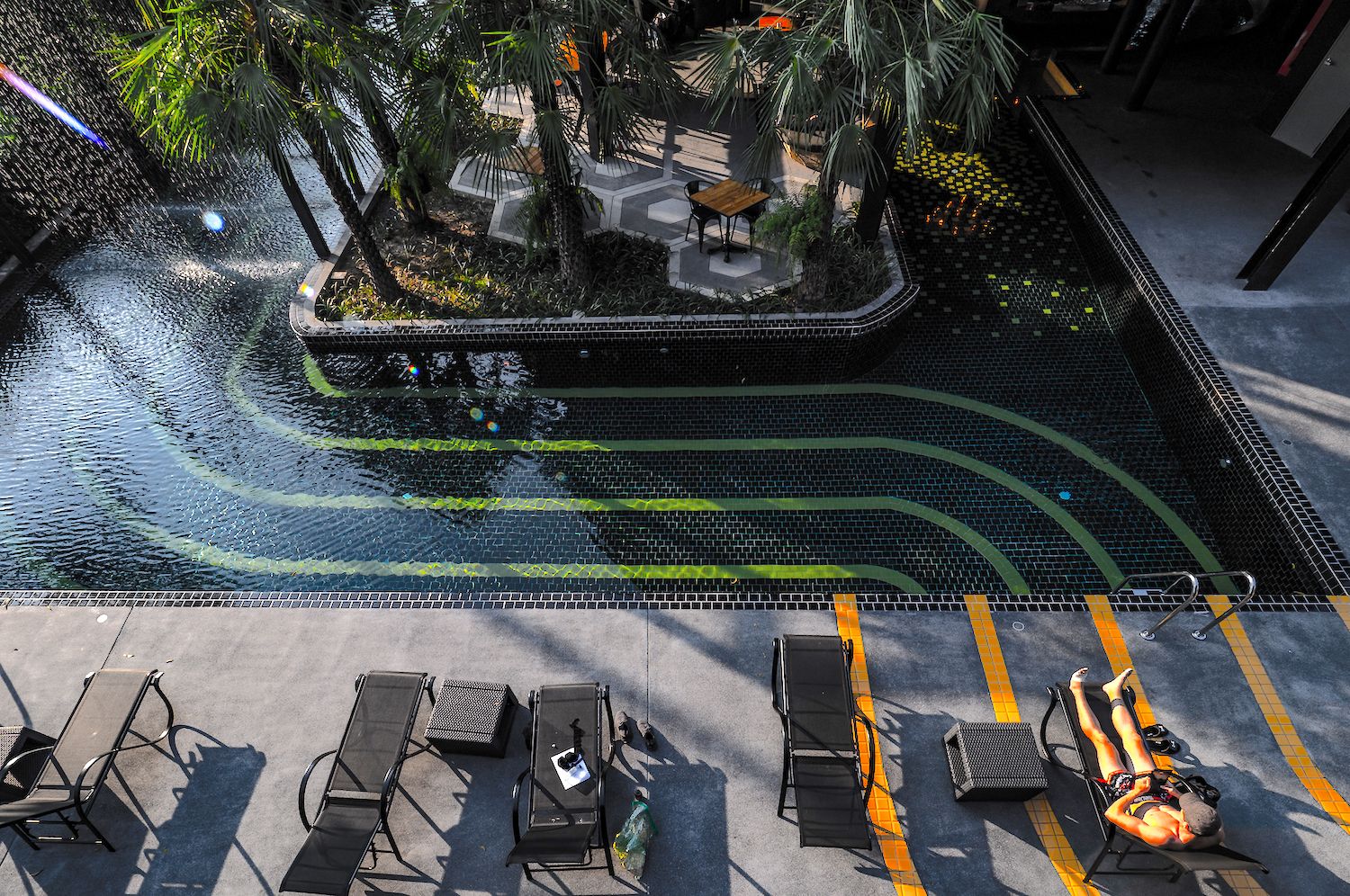 An outdoor pool area with lounge chairs and a small seating area surrounded by palm trees.
