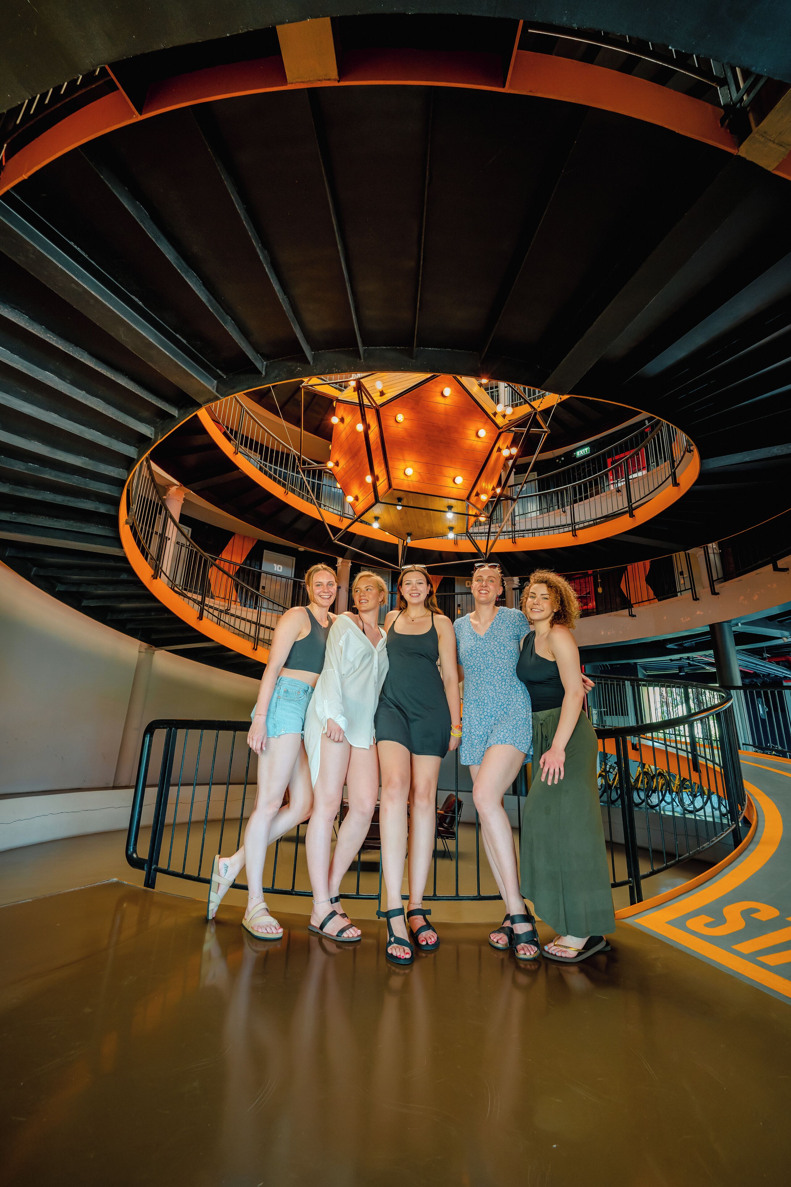 Een groep mensen staat in een modern, rond atrium met een centrale lamp en een spiraalvormige trap.