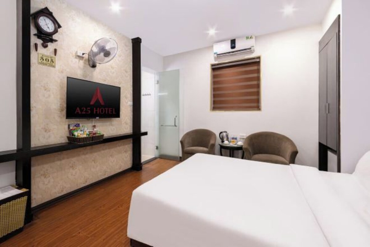 Habitación de hotel con cama, dos sillones, una mesita, televisión, aire acondicionado, un reloj y ventilador de pared.