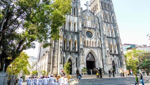 Une cathédrale historique dotée d’une grande horloge, entourée d’arbres et d’un groupe de personnes.