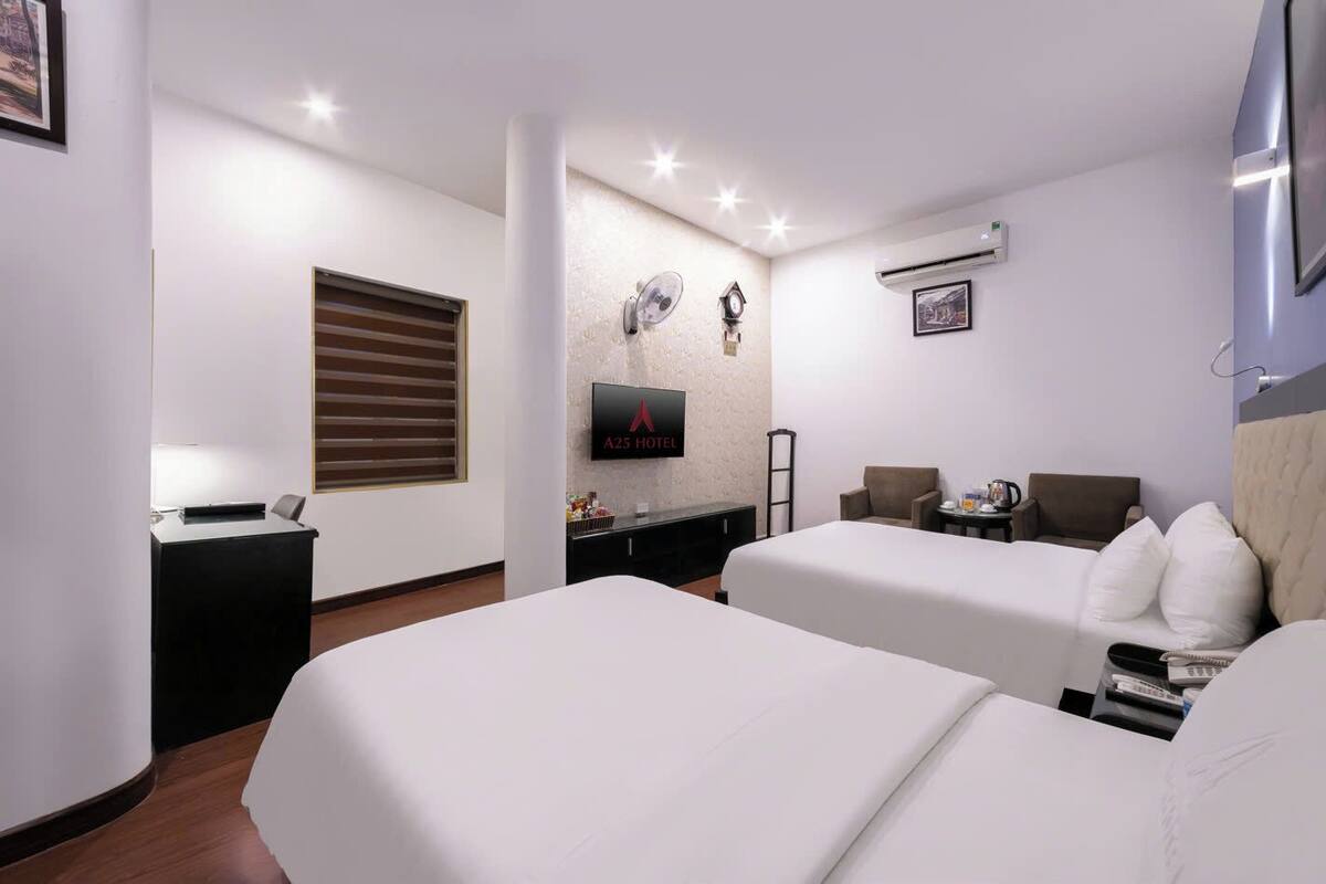 A hotel room with two beds, a TV, a small table, and a chair.