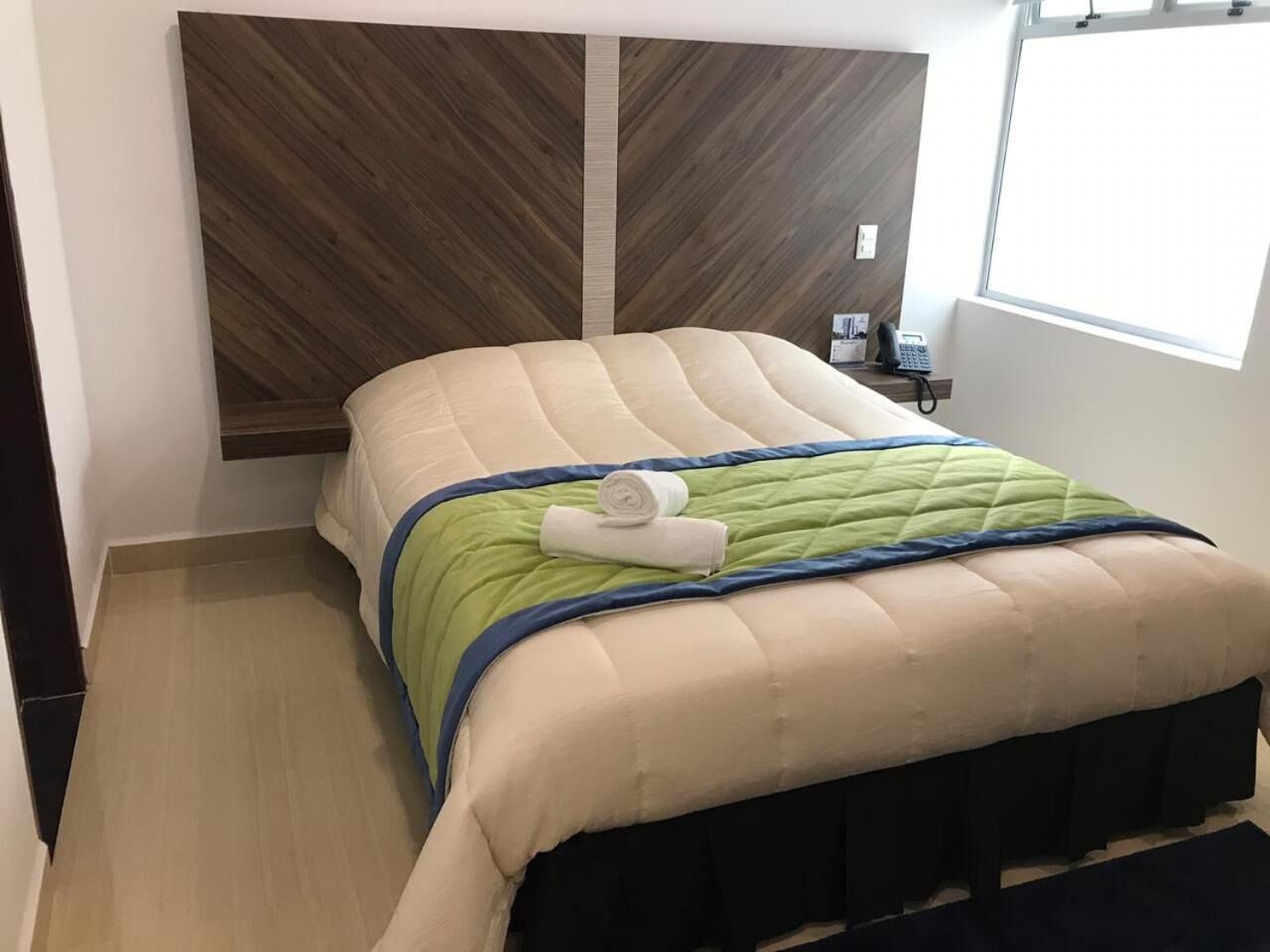 A bedroom with a bed, a bedside table with a phone, and a window.