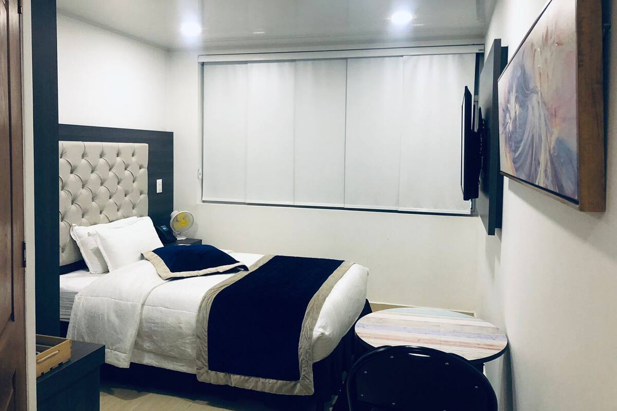 Un dormitorio con cama, mesita de noche y ventana con persianas.