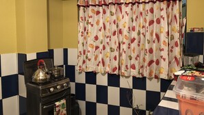 Una cocina con piso a cuadros, estufa, tetera y cortina con estampado de frutas.