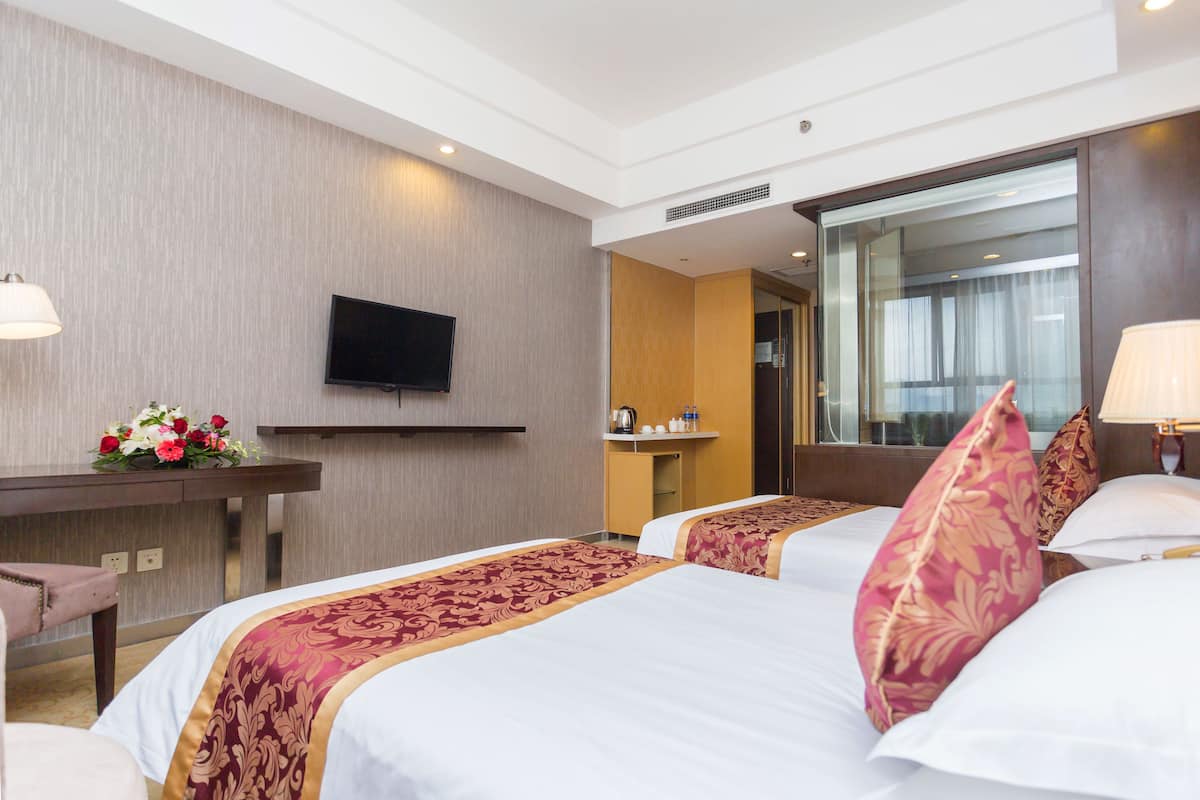 Une chambre d’hôtel avec deux lits, un bureau doté d’un téléviseur à écran plat, un miroir et une salle de bain visible à travers une porte ouverte.