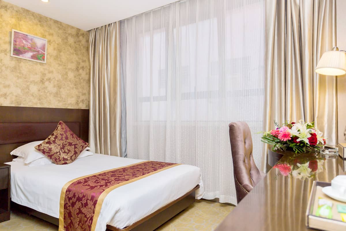 Une chambre d’hôtel avec un grand lit, une table de chevet, un bureau avec une lampe et un vase de fleurs.